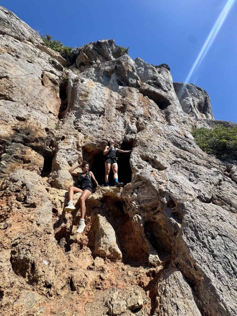 Baix Hike Mallorca hikers climbing rocky cliff with cave, adventure trekking and rugged coastal landscape