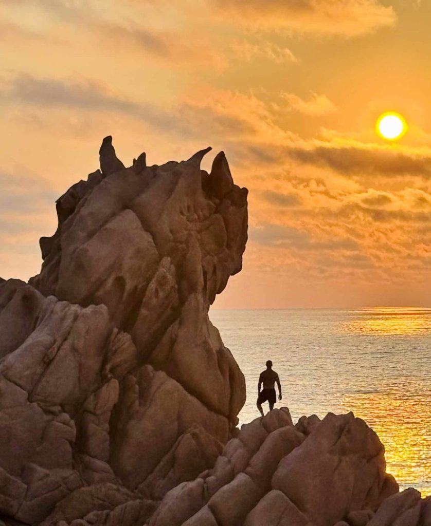 Coastal Advanced Hike: Sardinia sunset over sea with hiker on rocky cliffs, dramatic coastline and golden light panorama