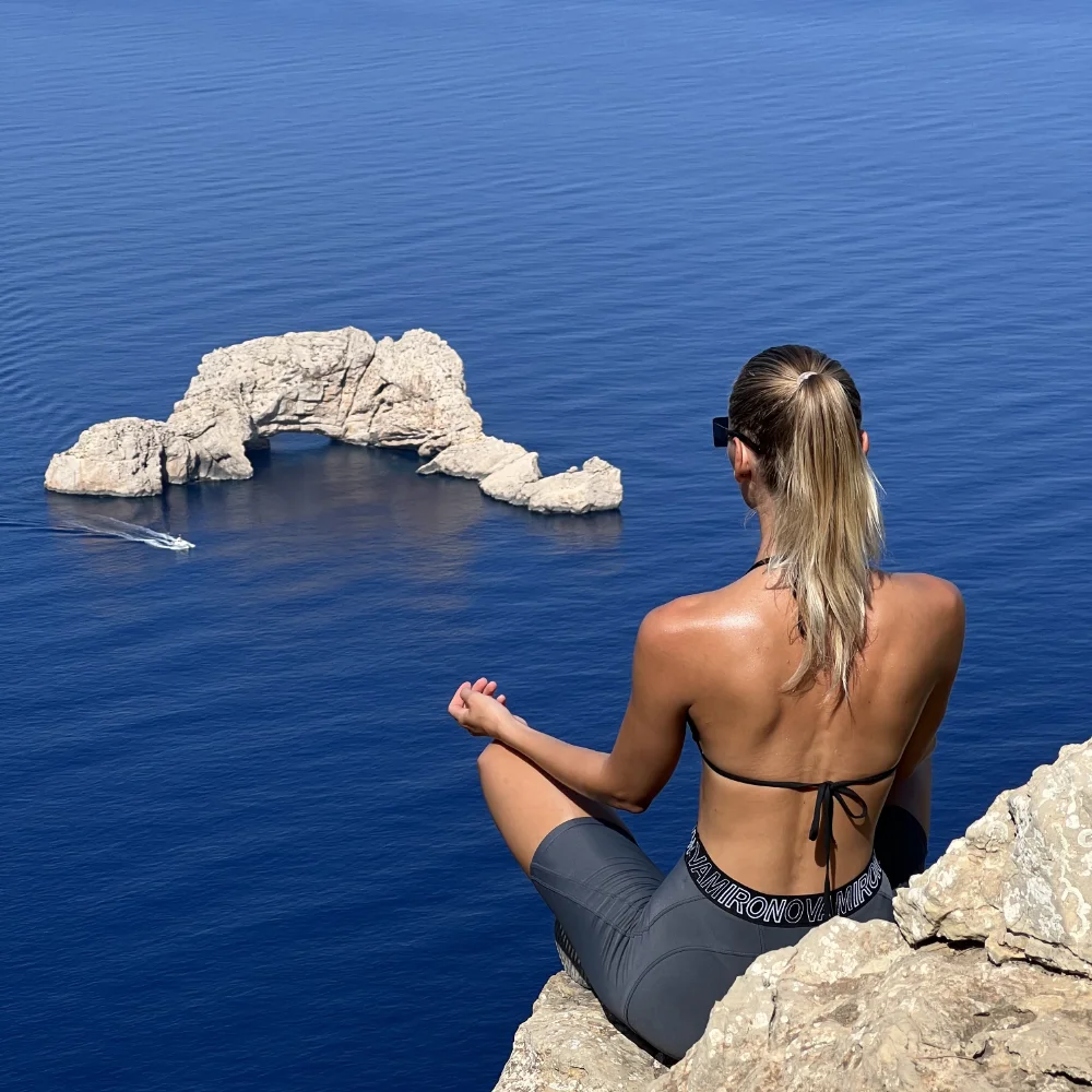 Hiker meditating in the sun on a cliff with sea view